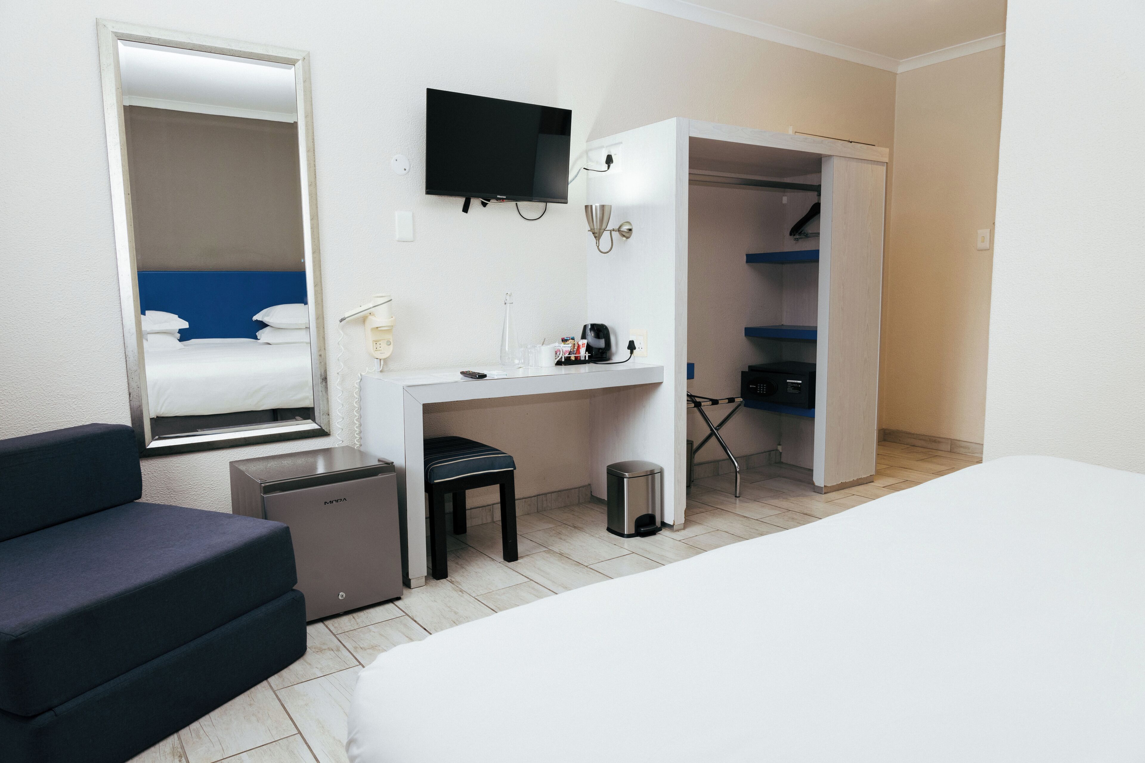 A hotel room with a bed, a desk, a chair, a TV, a wardrobe, and a small trash bin.