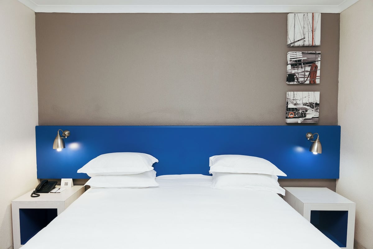 A hotel room with a large bed, two bedside tables, a blue headboard, and wall-mounted artwork.