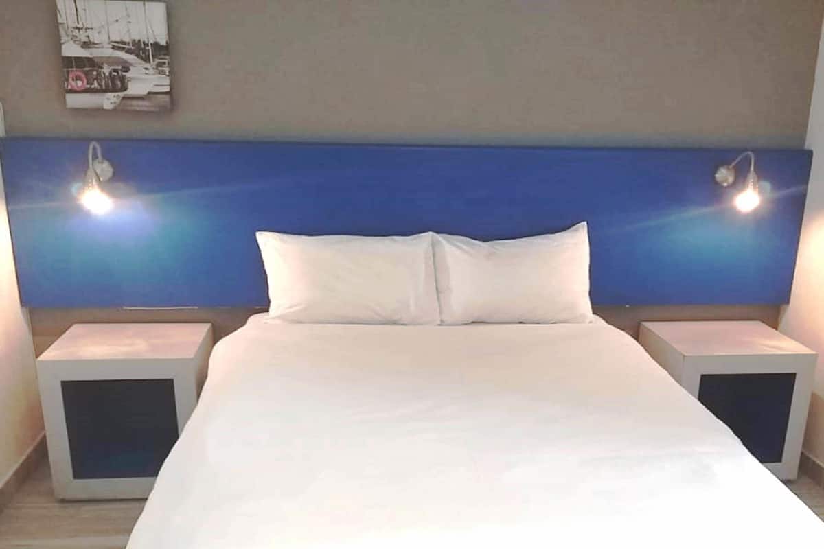 A hotel room with a large bed, two bedside tables, and a headboard with two wall-mounted lights.