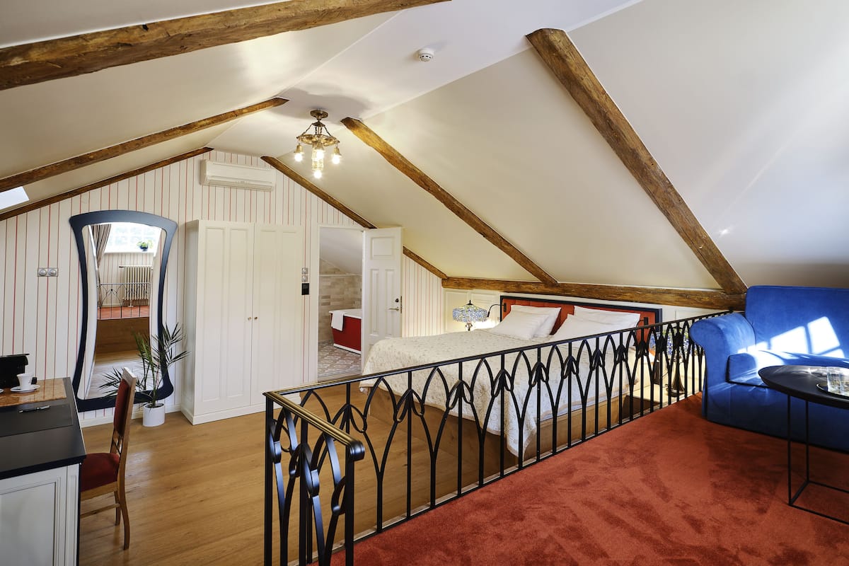 Une chambre spacieuse située sous les combles, avec un plafond en pente, un escalier en bois, une moquette rouge et un canapé bleu.