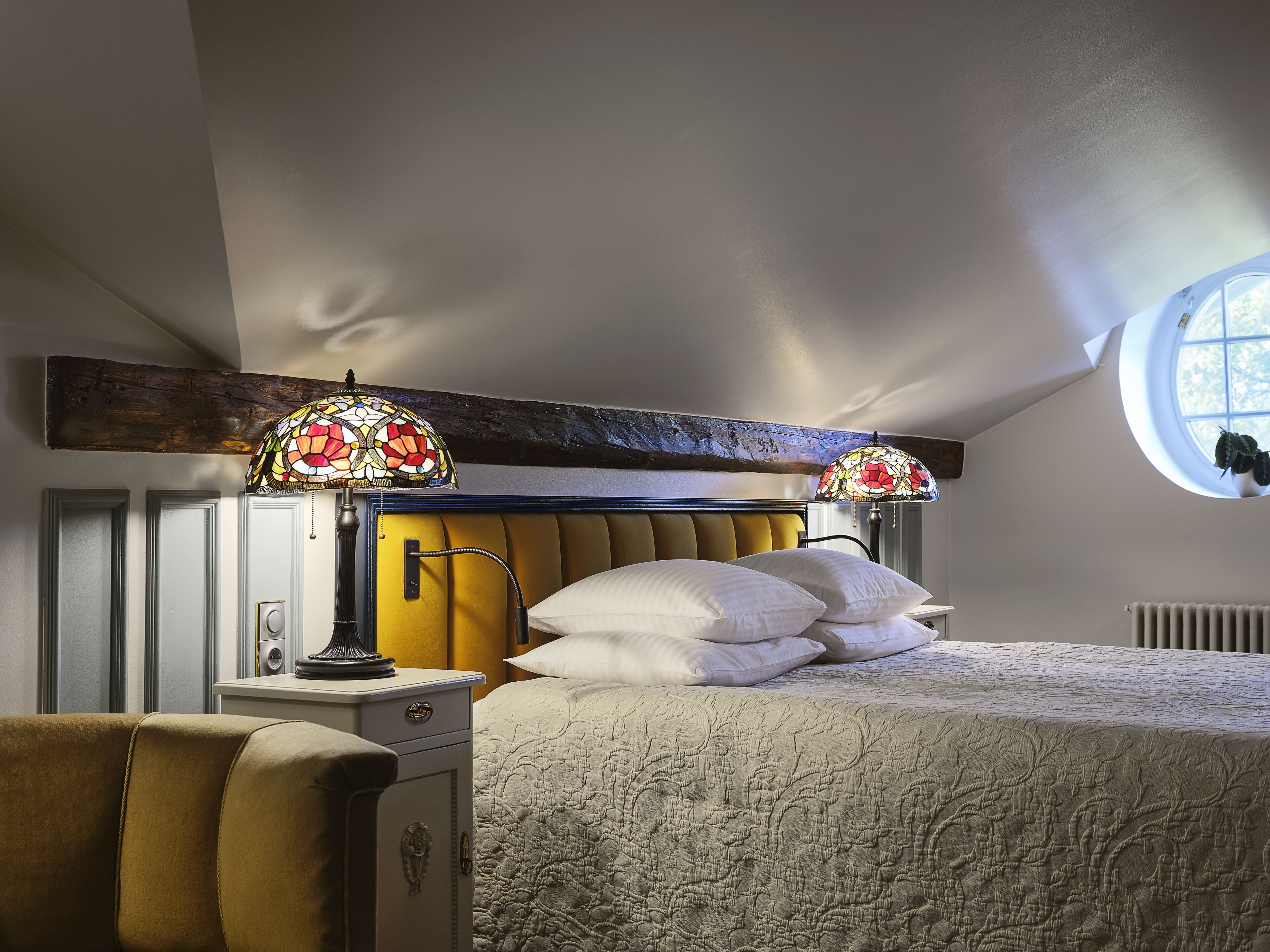 Quarto com cama, duas luminárias de cabeceira, mesa de cabeceira, uma cadeira e janela.