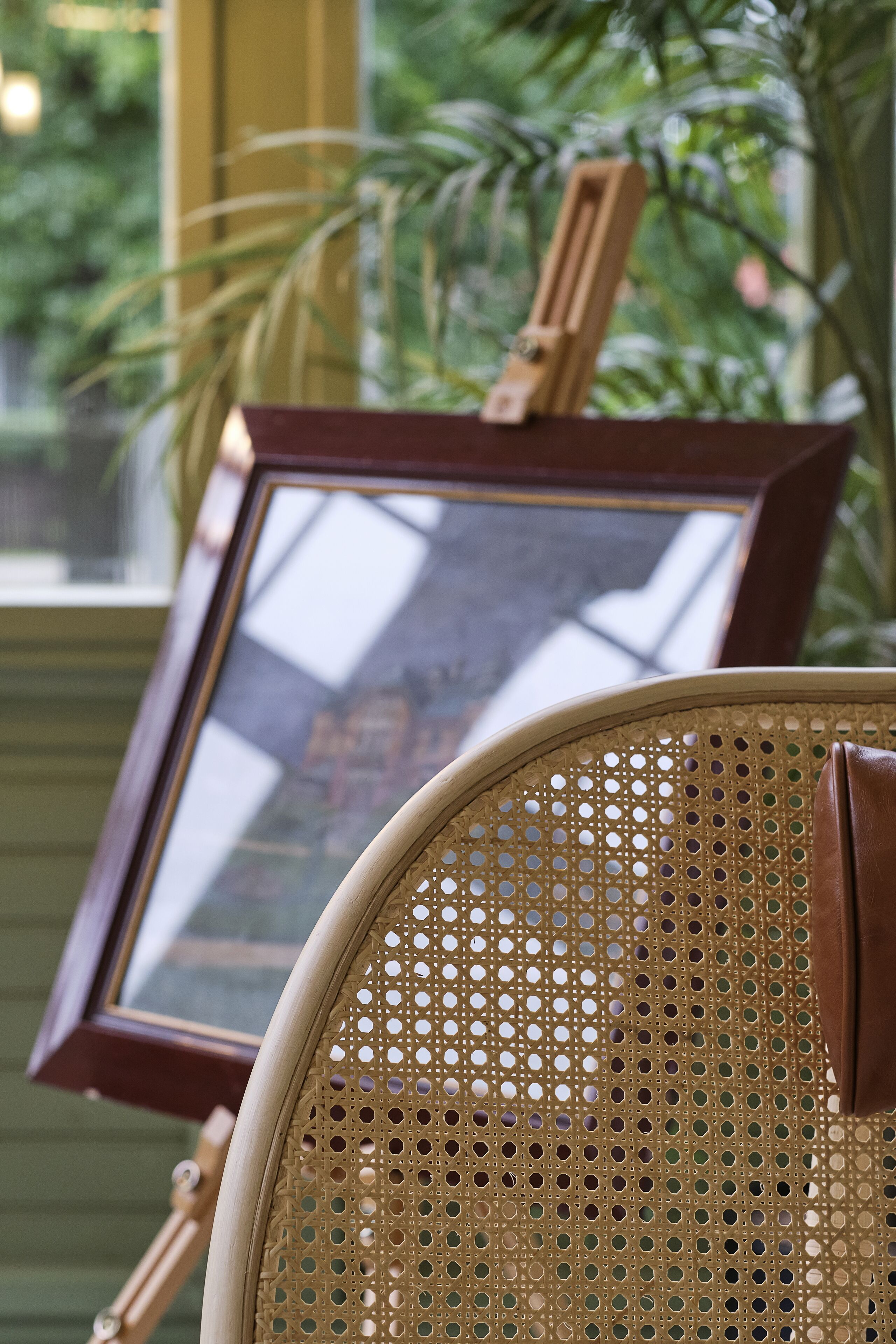 A wicker chair with a wooden frame and a picture frame leaning against a wall.