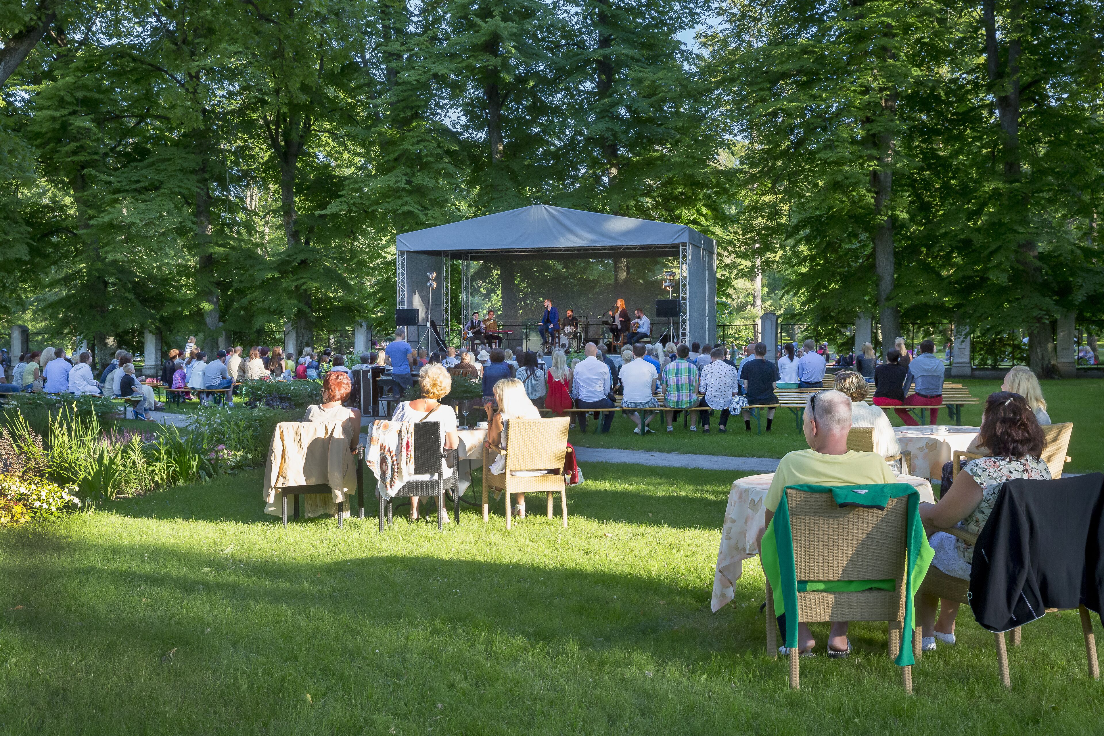 Katettu ulkoilmalava, jossa on istumapaikat yleisölle, ja se sijaitsee puistossa.
