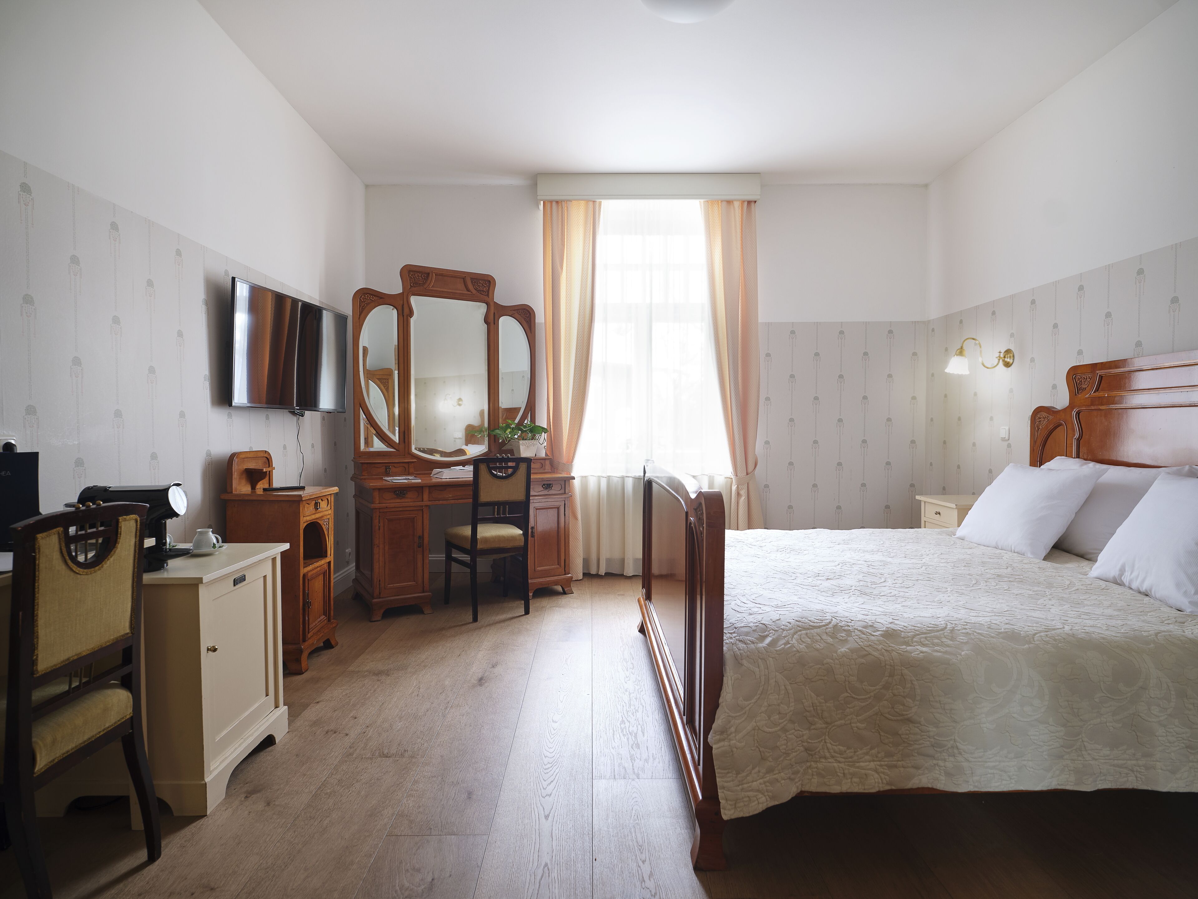 A bedroom with a wooden bed, a desk with a mirror, a television, and a dresser.
