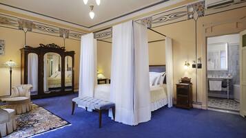 A bedroom with a four-poster bed, a sitting area with a bench, a large mirror, and a bathroom with a sink and mirror.