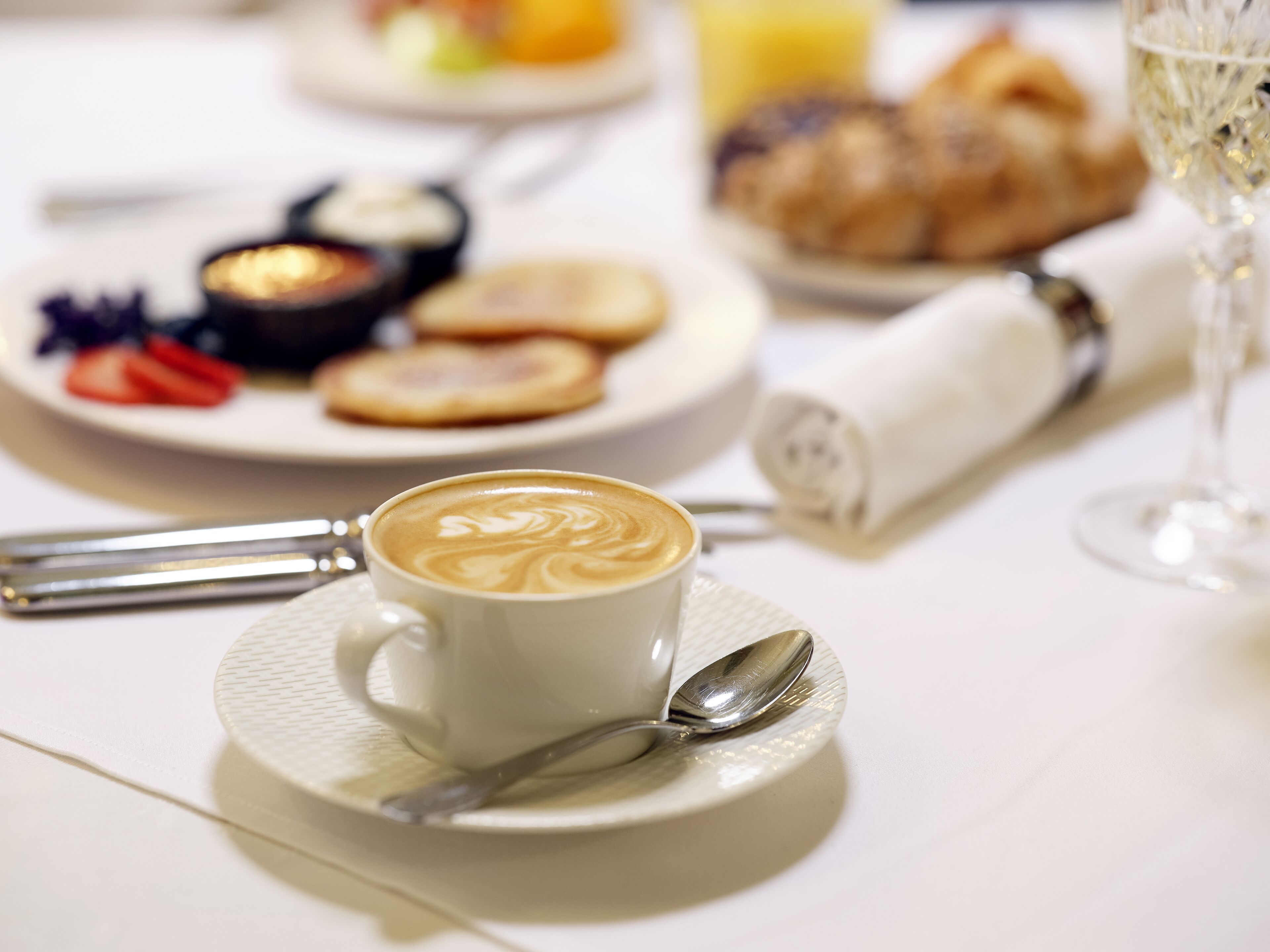 A breakfast setting with a cup of coffee, croissants, and a glass of orange juice on a table.