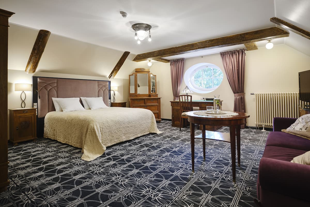 Une chambre à coucher avec un grand lit, une table ronde, une commode, un miroir, une fenêtre et un radiateur.