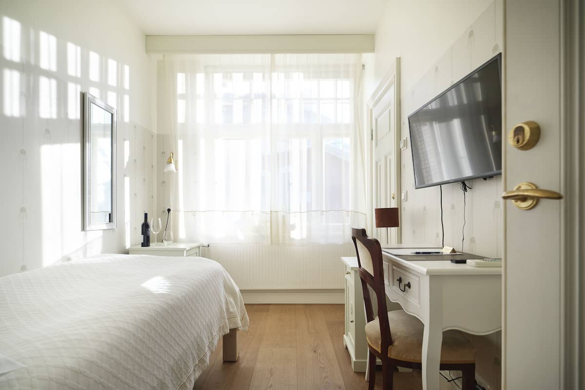 Une chambre à coucher avec un lit, un bureau, une chaise, une télévision et une fenêtre avec des rideaux.
