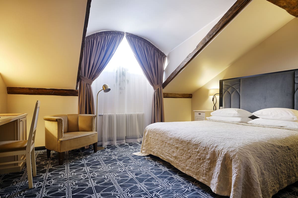 Une chambre d’hôtel avec un grand lit, une chaise, un bureau et une fenêtre avec des rideaux.