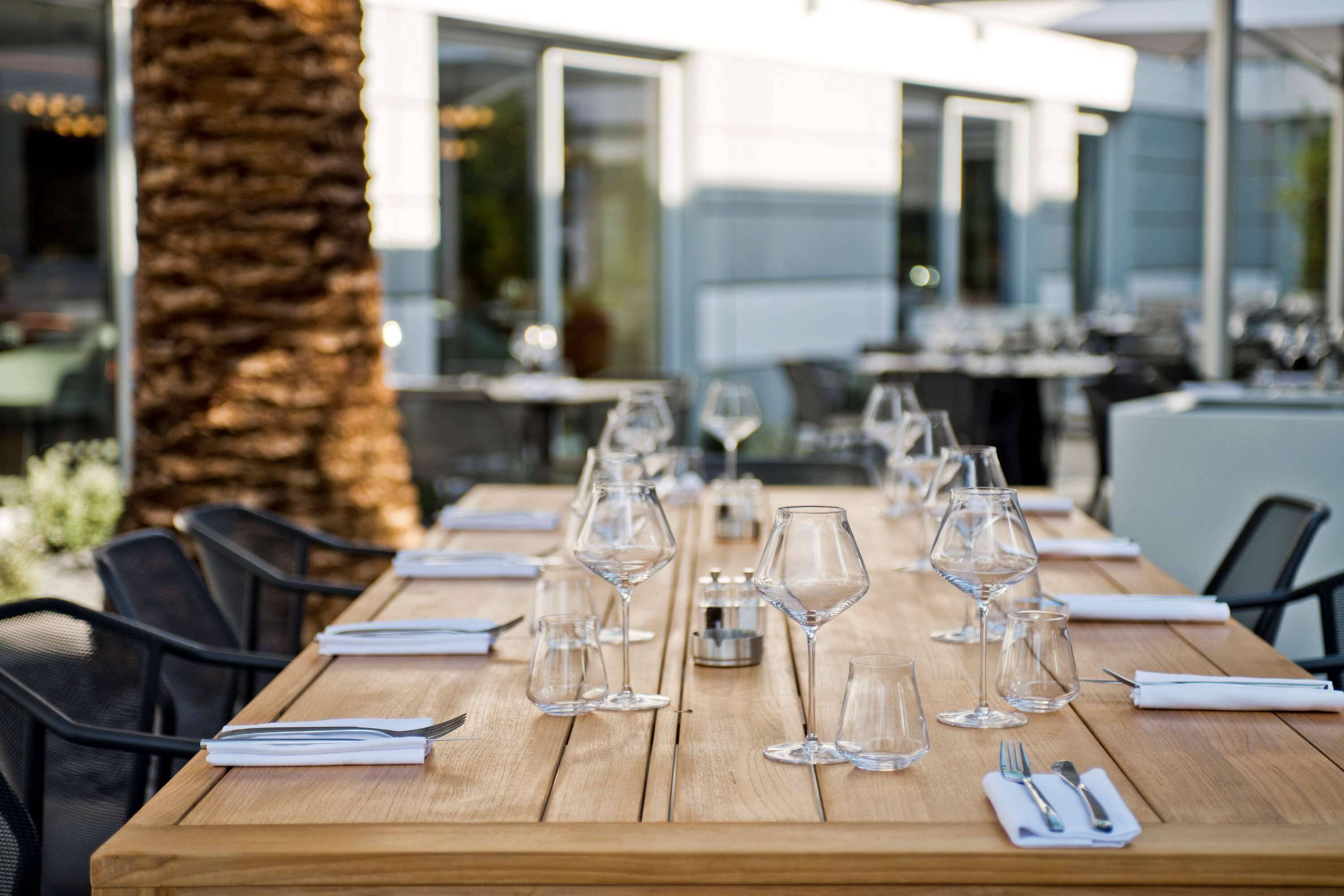 A wooden dining table set with multiple wine glasses and cutlery, surrounded by black chairs.