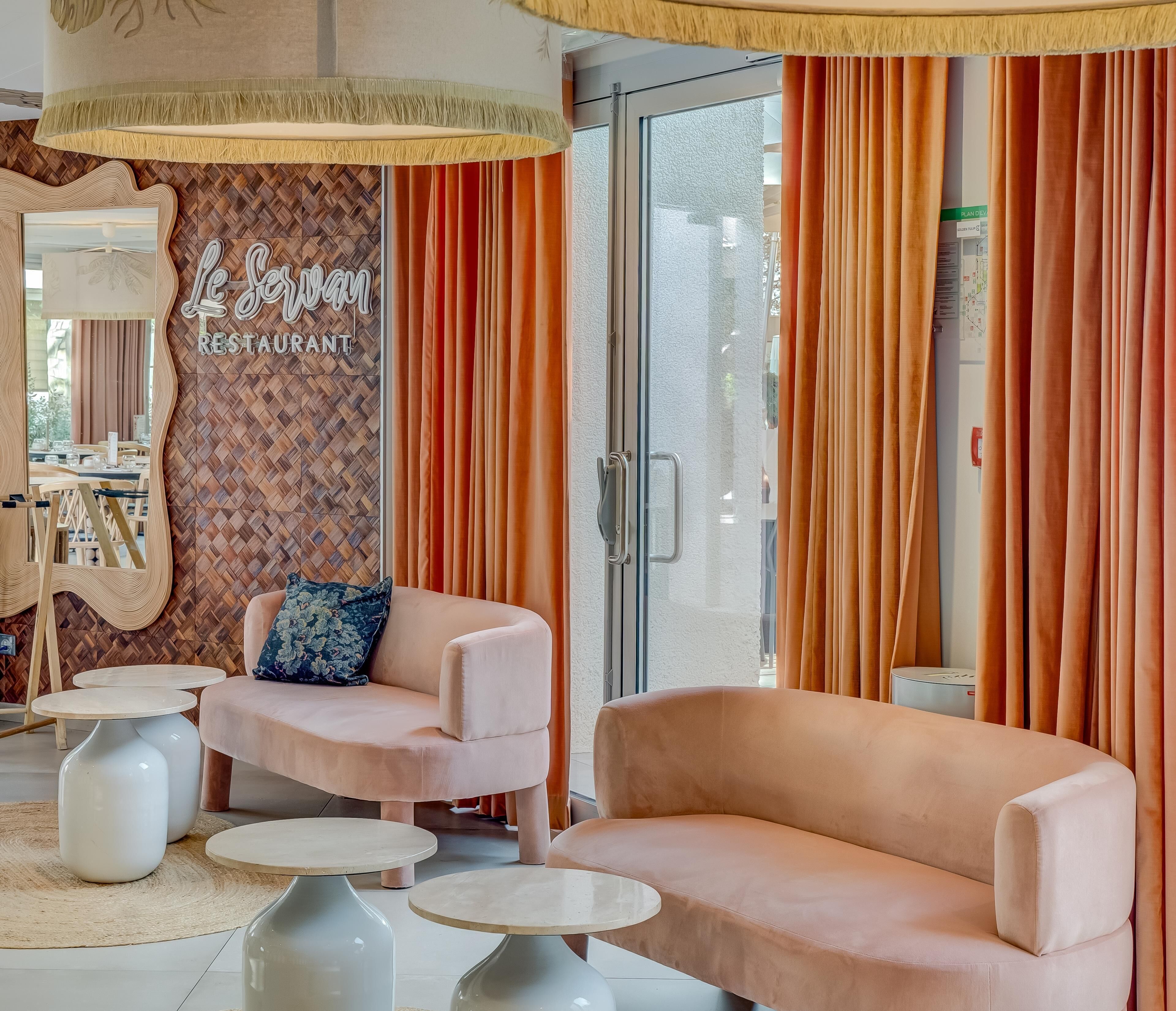 Una sala de estar moderna con sofá, sillón y una mesita de centro, una pared decorativa con el letrero de un restaurante y cortinas naranjas.