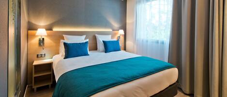 A hotel room with a bed, bedside tables, lamps, a window with curtains, and a view of greenery outside.