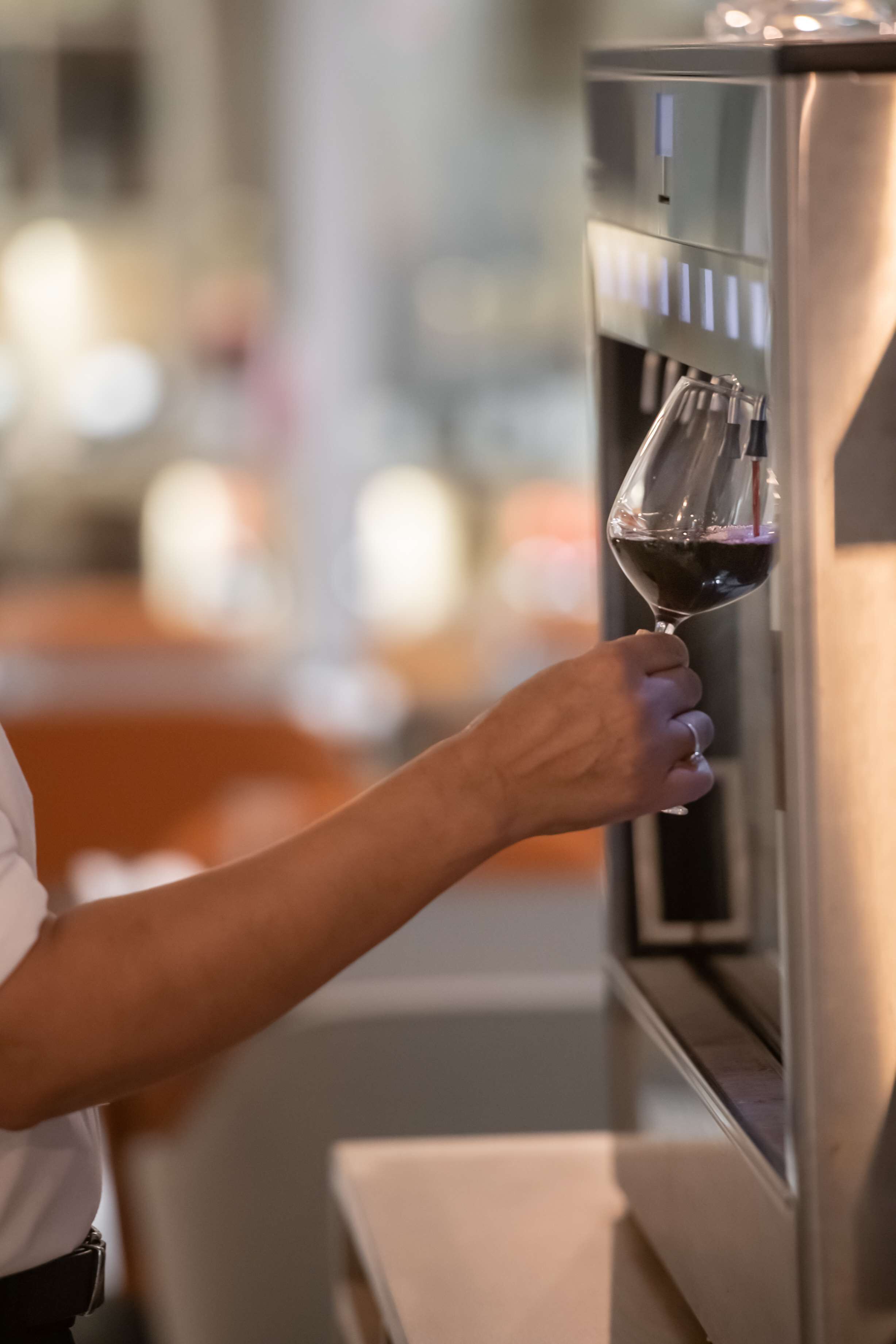 Une personne tenant un verre à vin près d’un distributeur de vin.