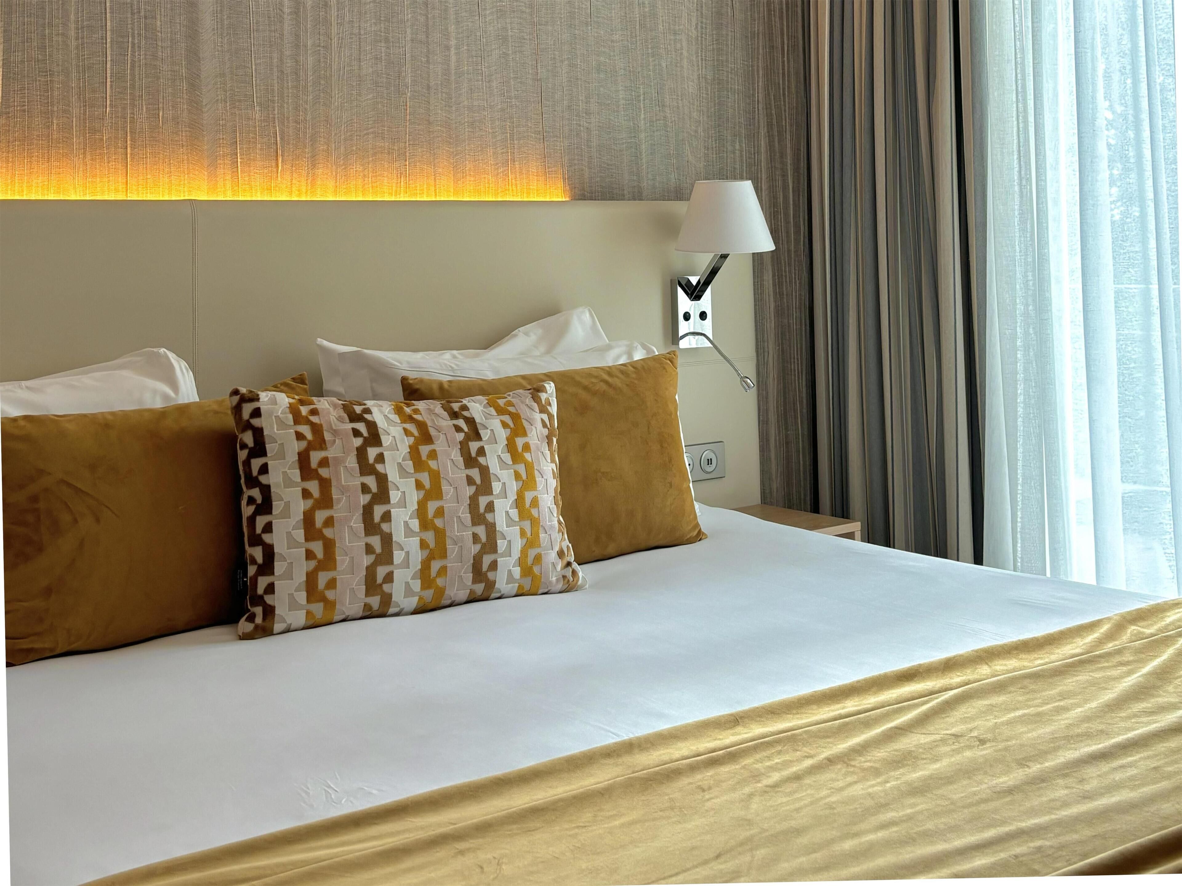 Una camera d'albergo con un letto, due cuscini, una lampada e una finestra con tende.