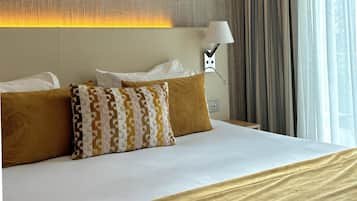 Una camera d'albergo con un letto, due cuscini, una lampada e una finestra con tende.
