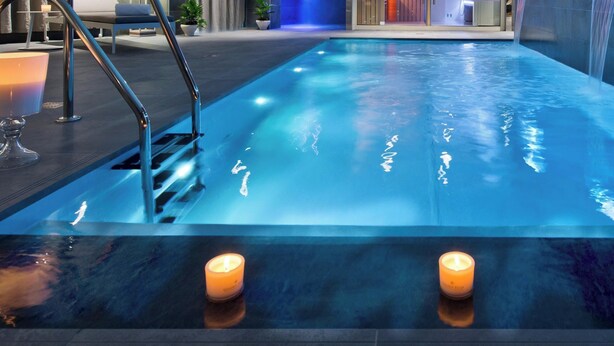 Una piscina con superficie de agua azul cristalina, un juego de escaleras y tres velas encendidas en el borde de la piscina.