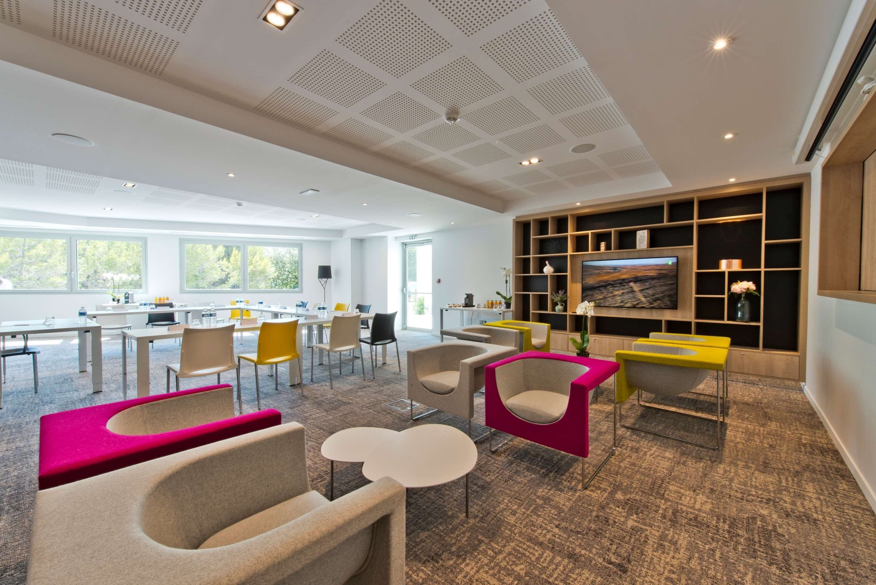 Un espacio de oficina moderno y bien iluminado, con un televisor grande, asientos cómodos y una cocina visible.