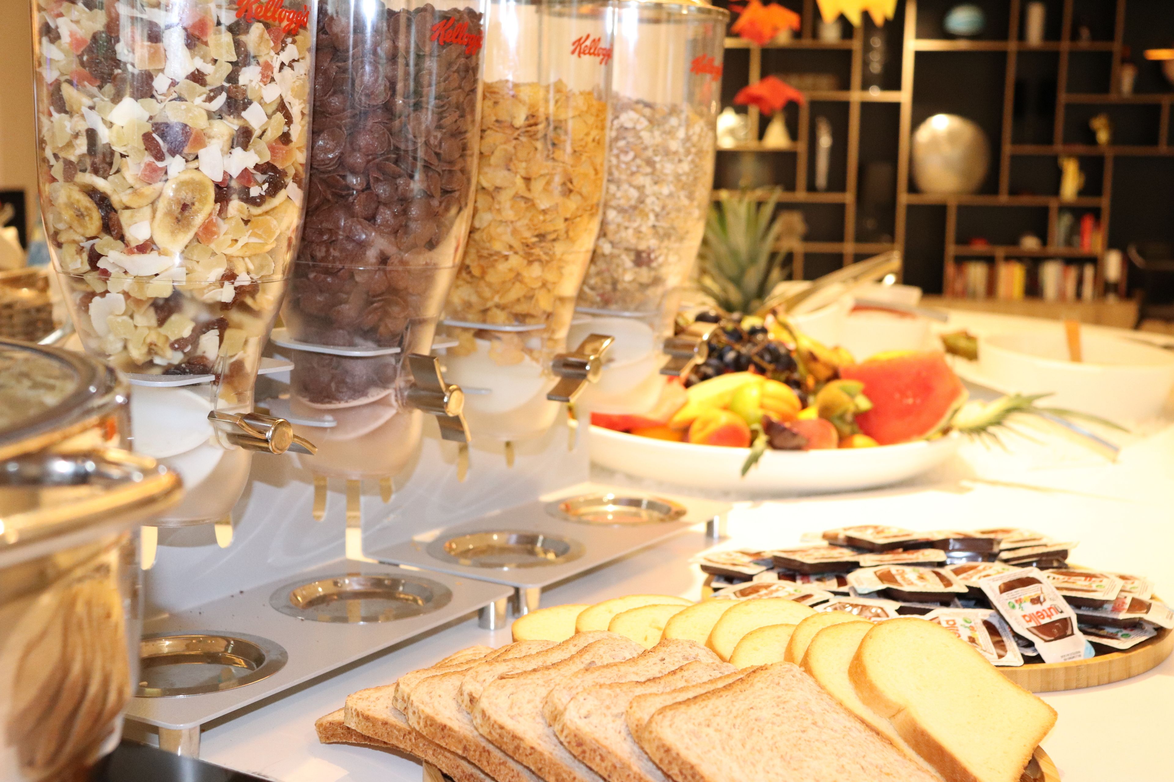En buffet med et udvalg af madmuligheder, herunder müsli, frugt og sandwiches.