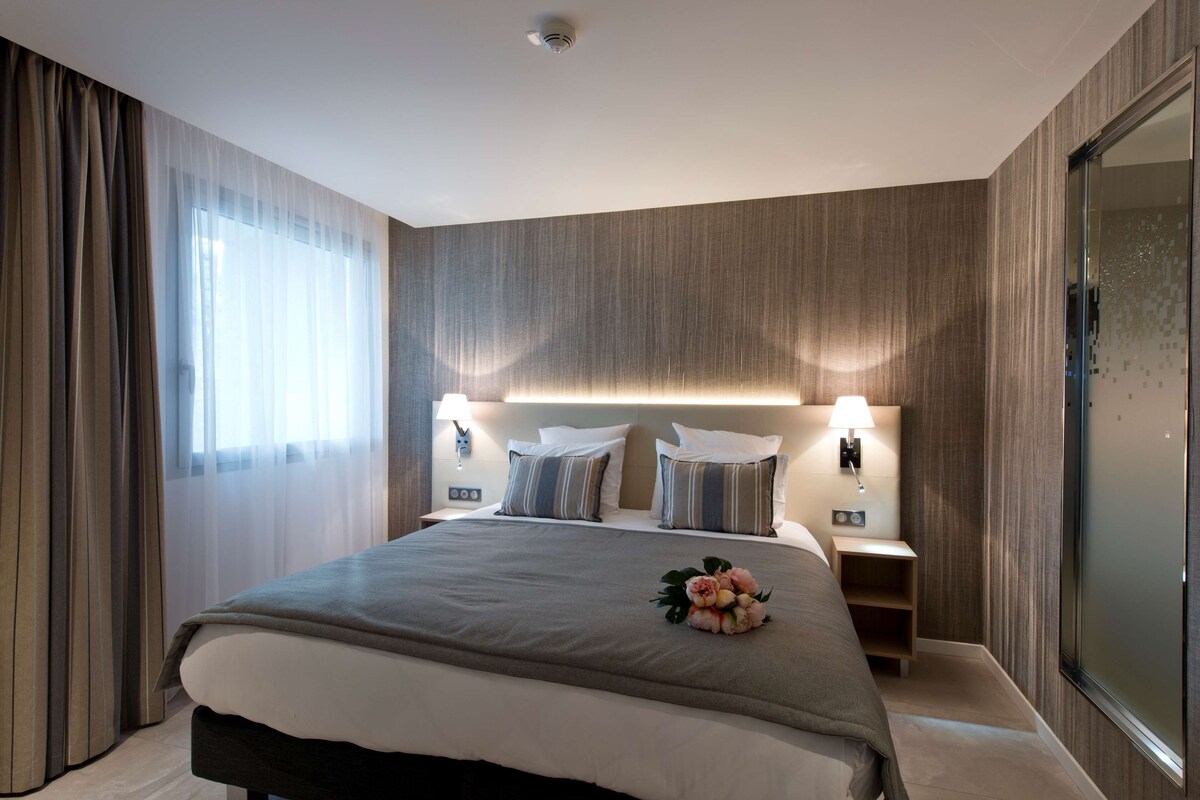 Quarto de hotel moderno com uma cama grande, duas mesas de cabeceira e um espelho.