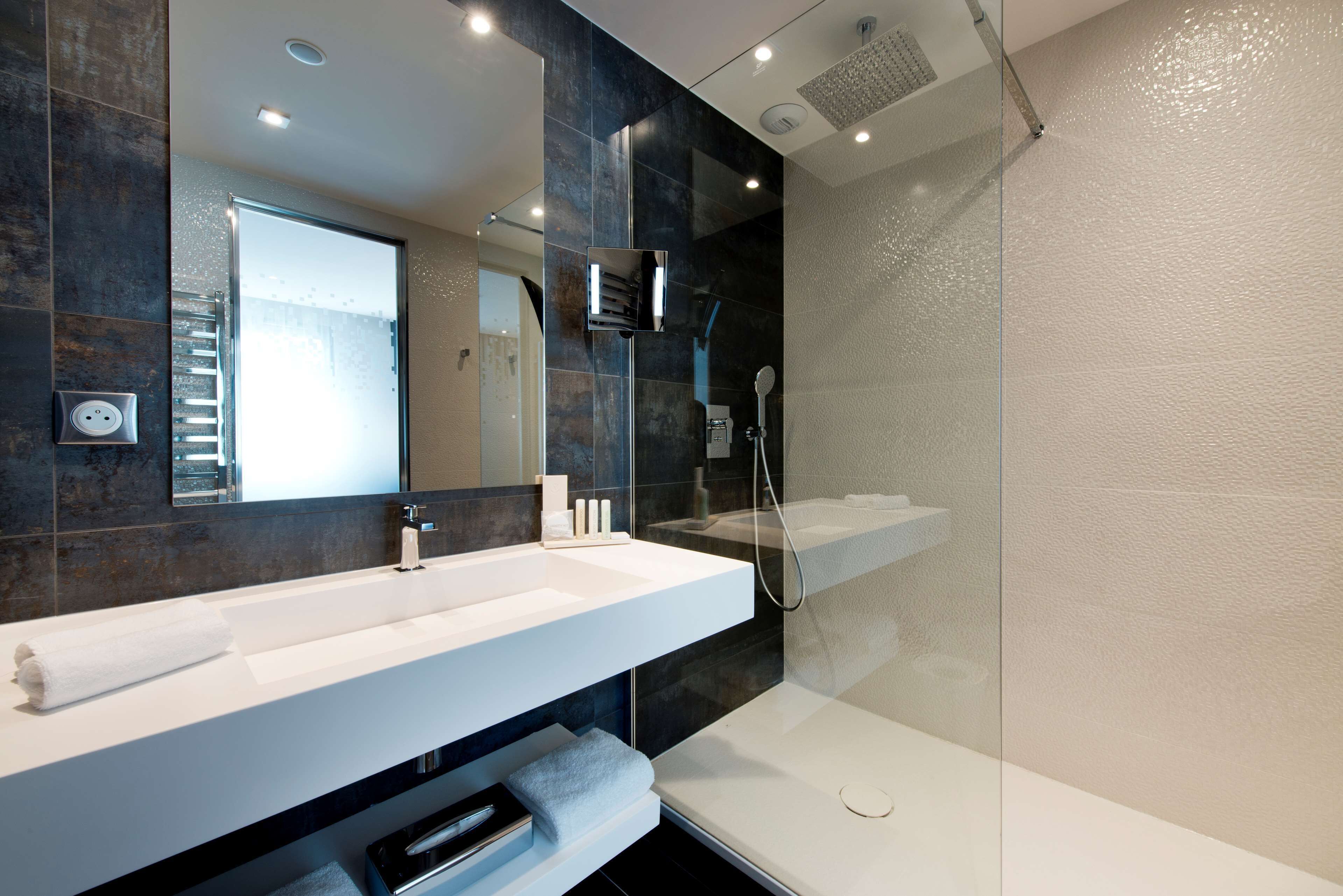 Une salle de bain moderne avec un grand miroir, un lavabo blanc et une douche à parois de verre.