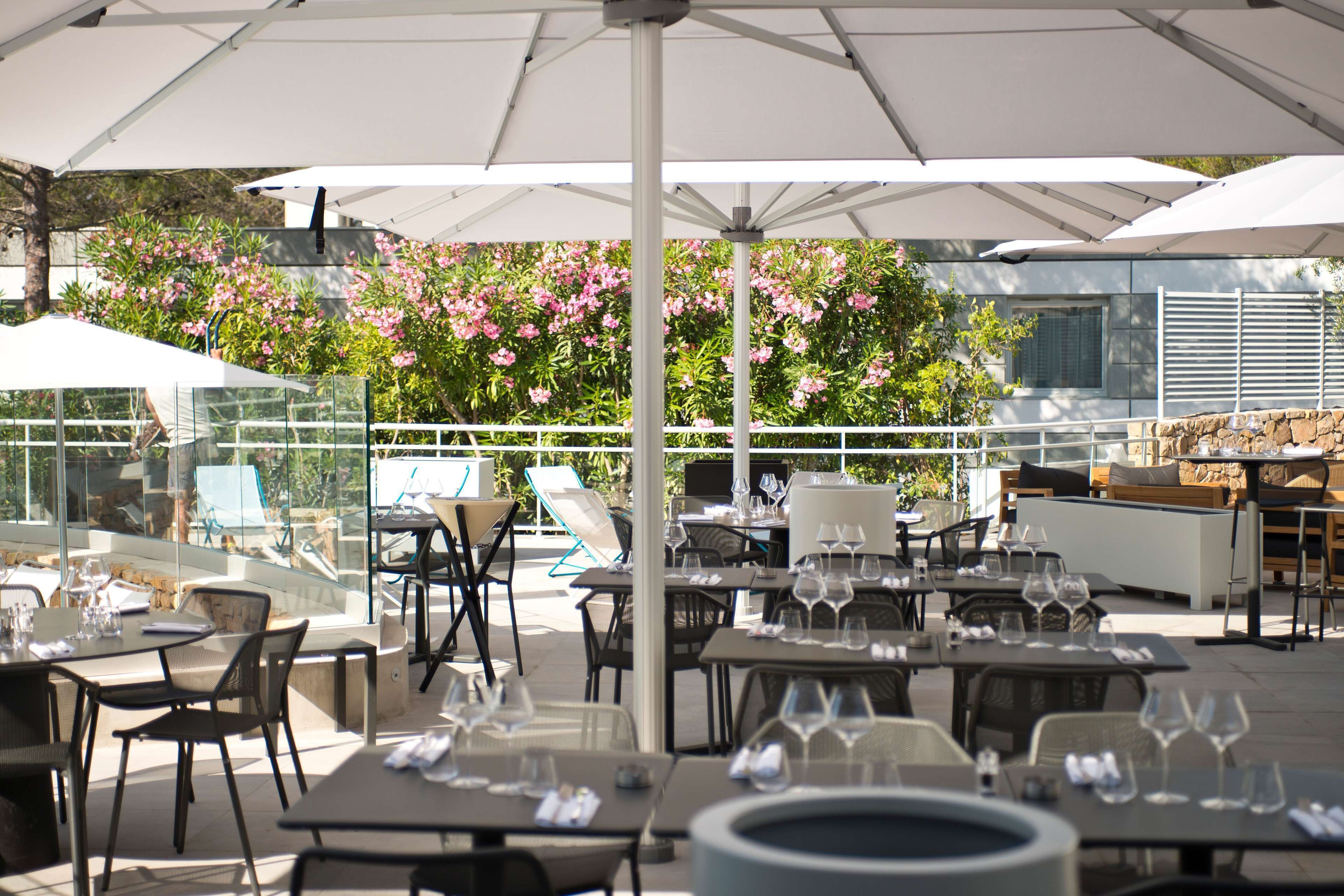 Un espace de restauration en plein air avec des tables et des chaises, des parasols et une vue sur des fleurs roses et de la verdure.