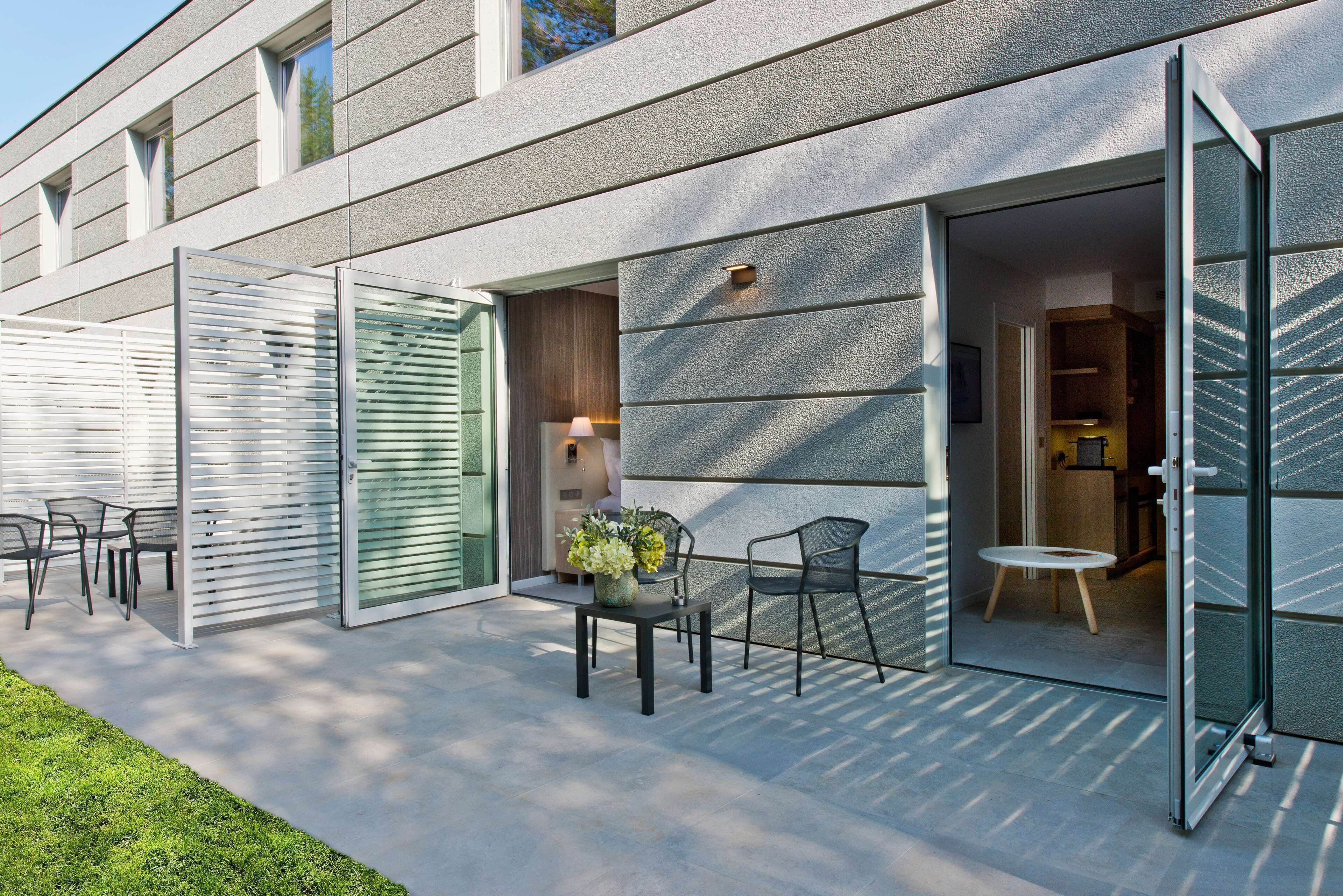An outdoor patio with a table and chairs, a small garden area, and a building entrance with glass doors.