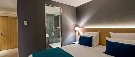 A hotel room with a bed, a nightstand, a lamp, a mirror, a door, and a shower area.