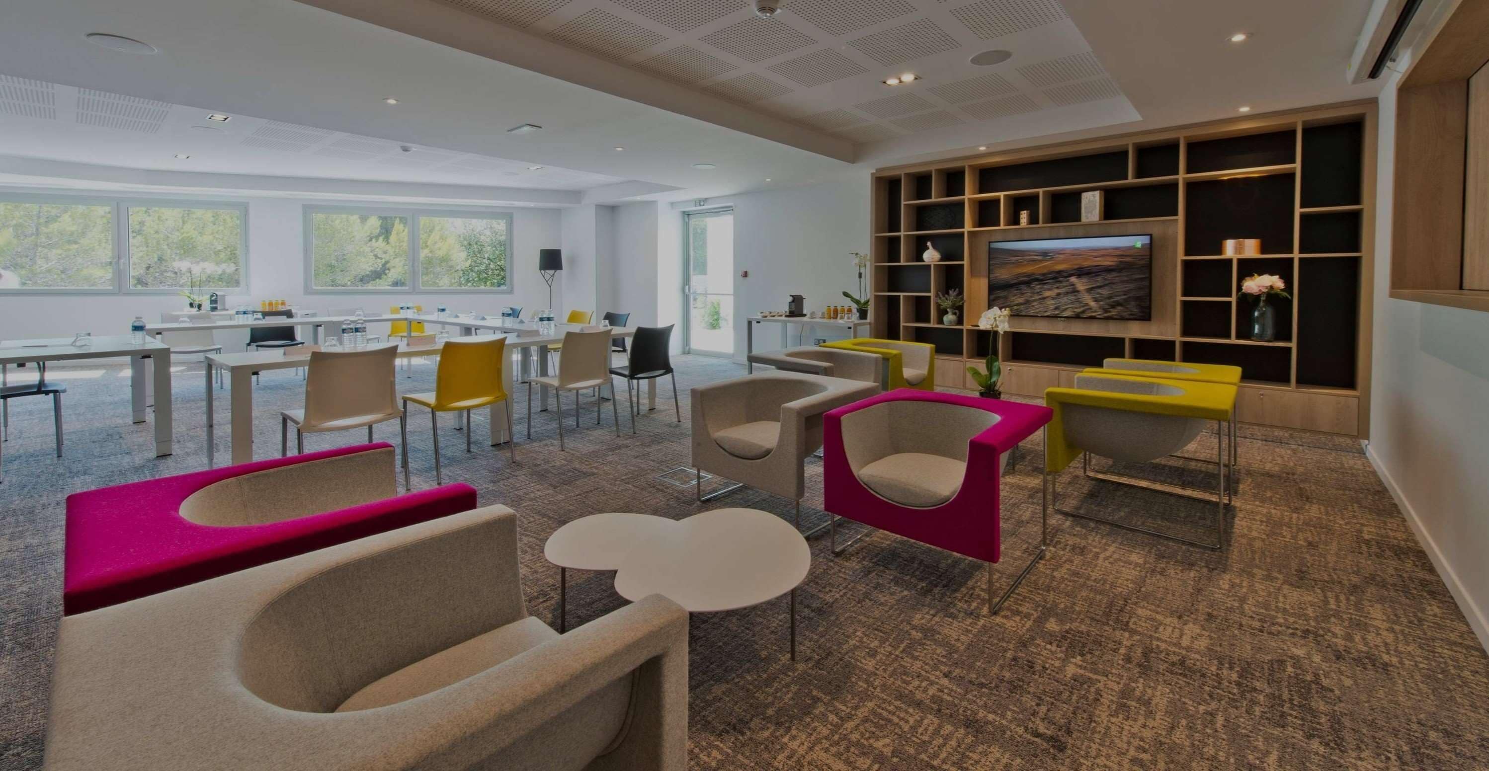 A modern conference room with a large table, multiple chairs, a television, and a bookshelf.