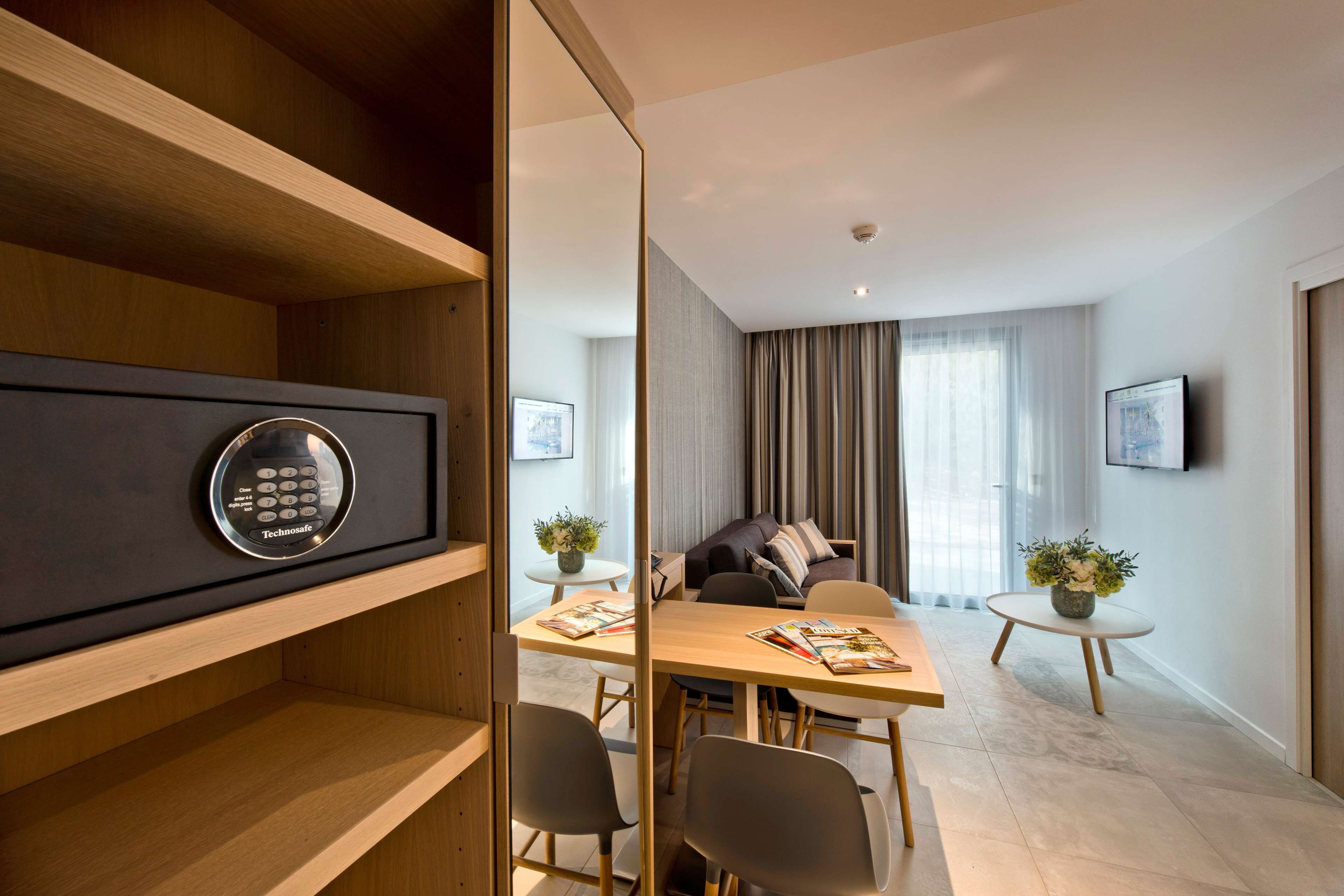 A modern hotel room with a wooden desk, a sofa, and a TV mounted on the wall.