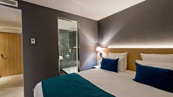 A hotel room with a bed, a nightstand, a lamp, a mirror, and a door leading to a bathroom.