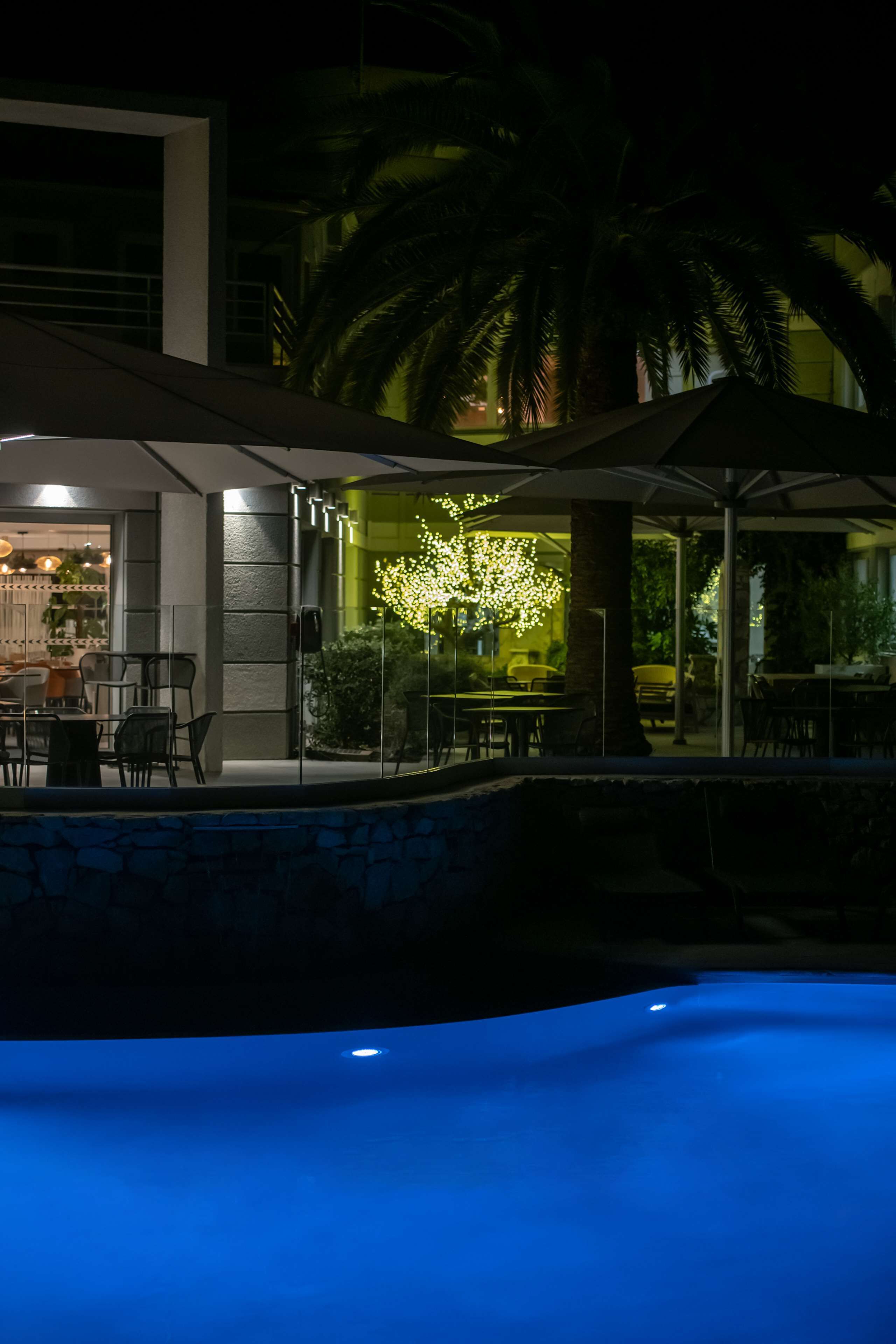 Un espace piscine extérieur doté d’un bar et de coins salon, entouré de palmiers et agrémenté d’une terrasse bien éclairée.
