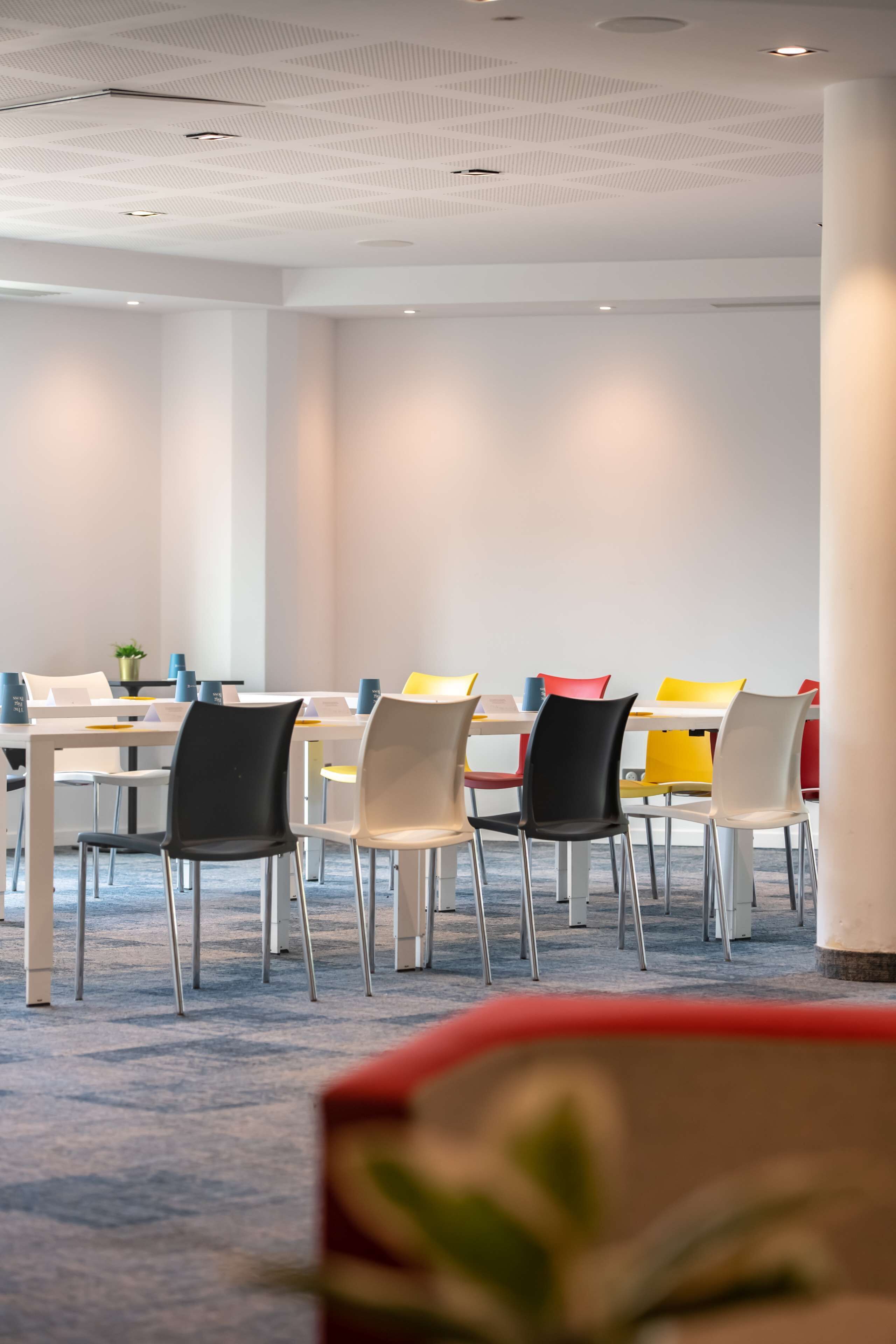 A conference room with a long table and chairs, white walls, and a ceiling with a geometric pattern.