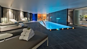 Un área de piscina interior moderna con sillones de descanso, una piscina pequeña e iluminación ambiental.