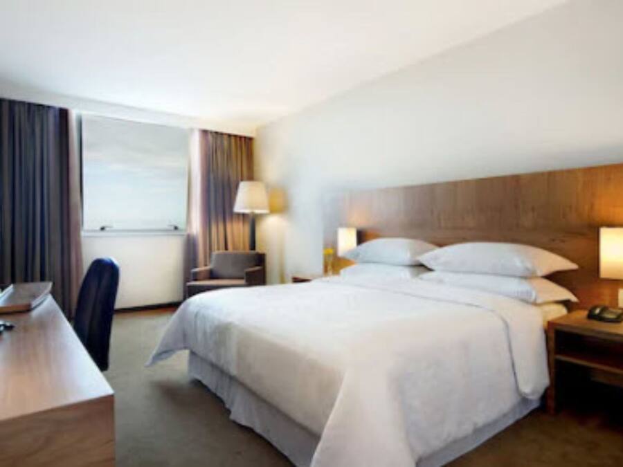 A hotel room with a large bed, a desk with a computer, a chair, and a window with curtains.