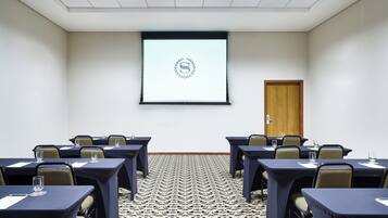 A conference room with tables and chairs, a projector screen, and a patterned carpet.