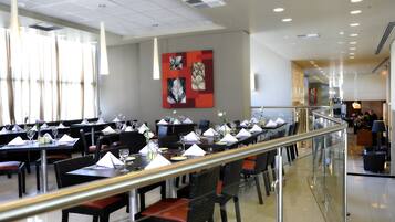 A spacious dining area with multiple tables and chairs, a glass railing, and a modern ceiling design.