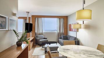 Quarto de hotel moderno com uma escrivaninha de madeira, uma mesa redonda de mármore, um sofá e uma TV fixada na parede.