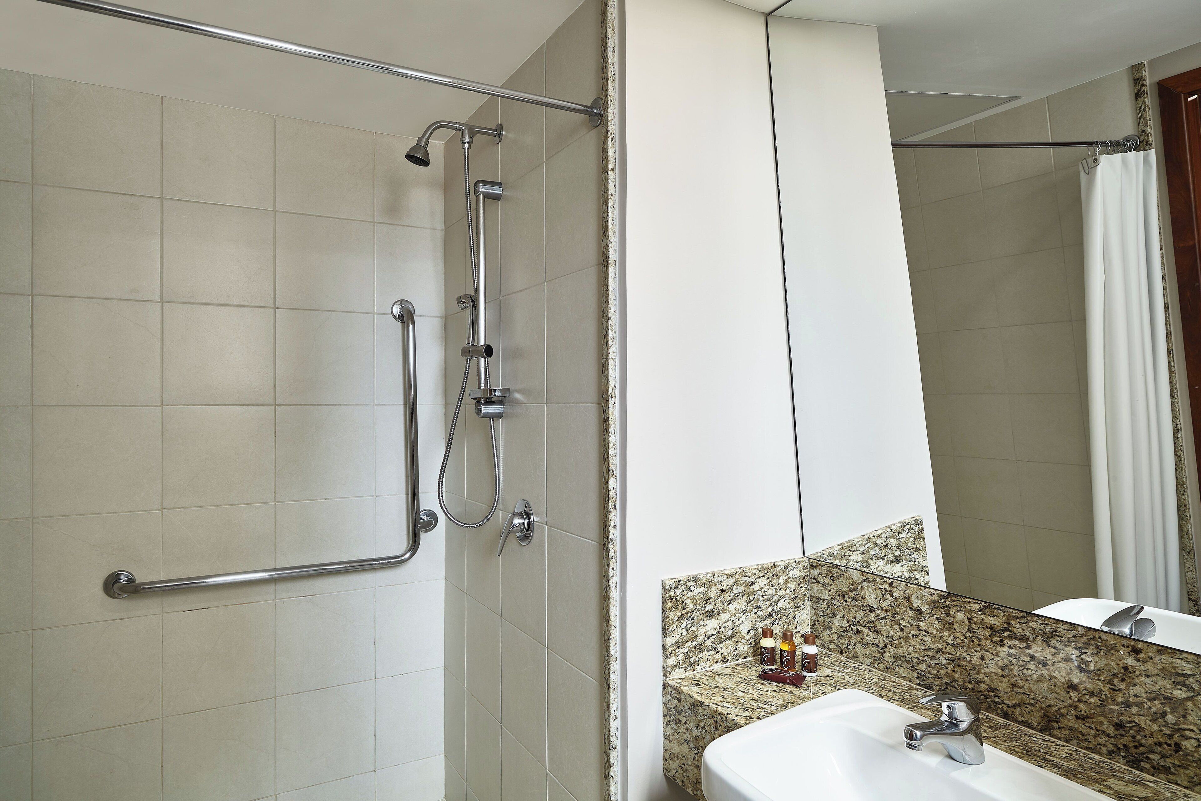 A bathroom with a shower, grab bar, sink, and mirror.