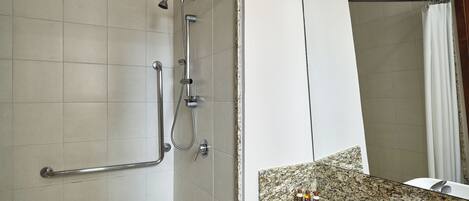 Un baño con ducha, barra de apoyo, lavamanos y espejo.