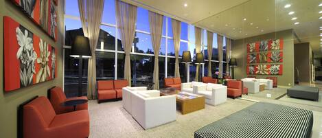 A modern hotel lobby with large windows, red and white sofas, and a large striped rug.