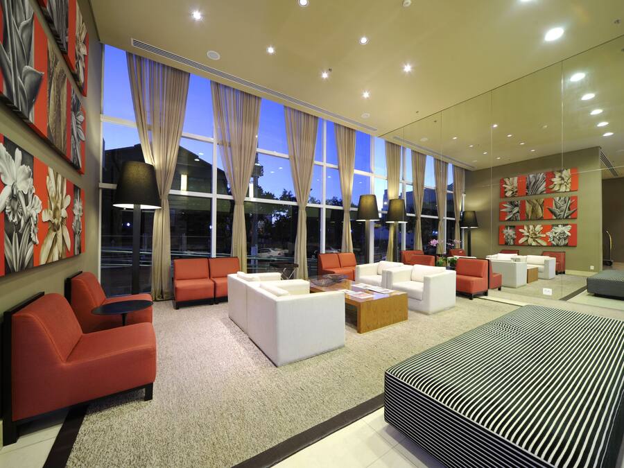 Un moderno vestíbulo de hotel con amplias ventanas, sofás rojos y blancos, y una alfombra grande a rayas.