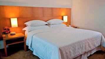 A neatly made bed with white linens, a wooden headboard, and two bedside lamps.