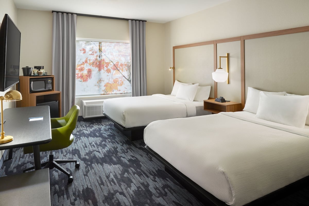 Een hotelkamer met twee bedden, een bureau, een stoel, een televisie en een raam met gordijnen.