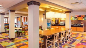 A hotel lobby with a central dining area, a kitchen, and a colorful carpet.