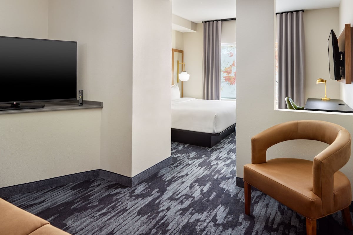 Een hotelkamer met een flatscreen televisie, een bed, een bureau met lamp en een stoel.