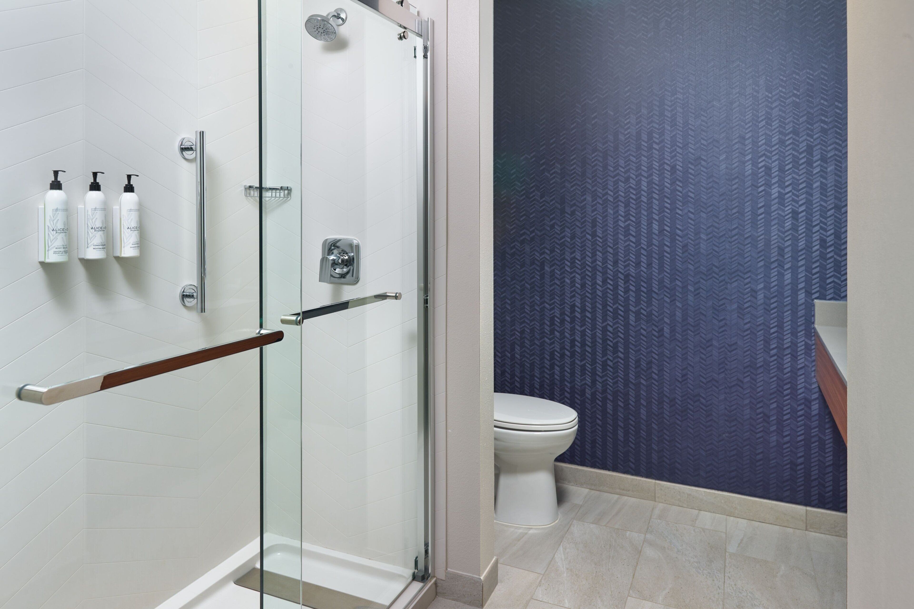 A modern bathroom with a glass-enclosed shower, a white toilet, and a blue patterned wall.