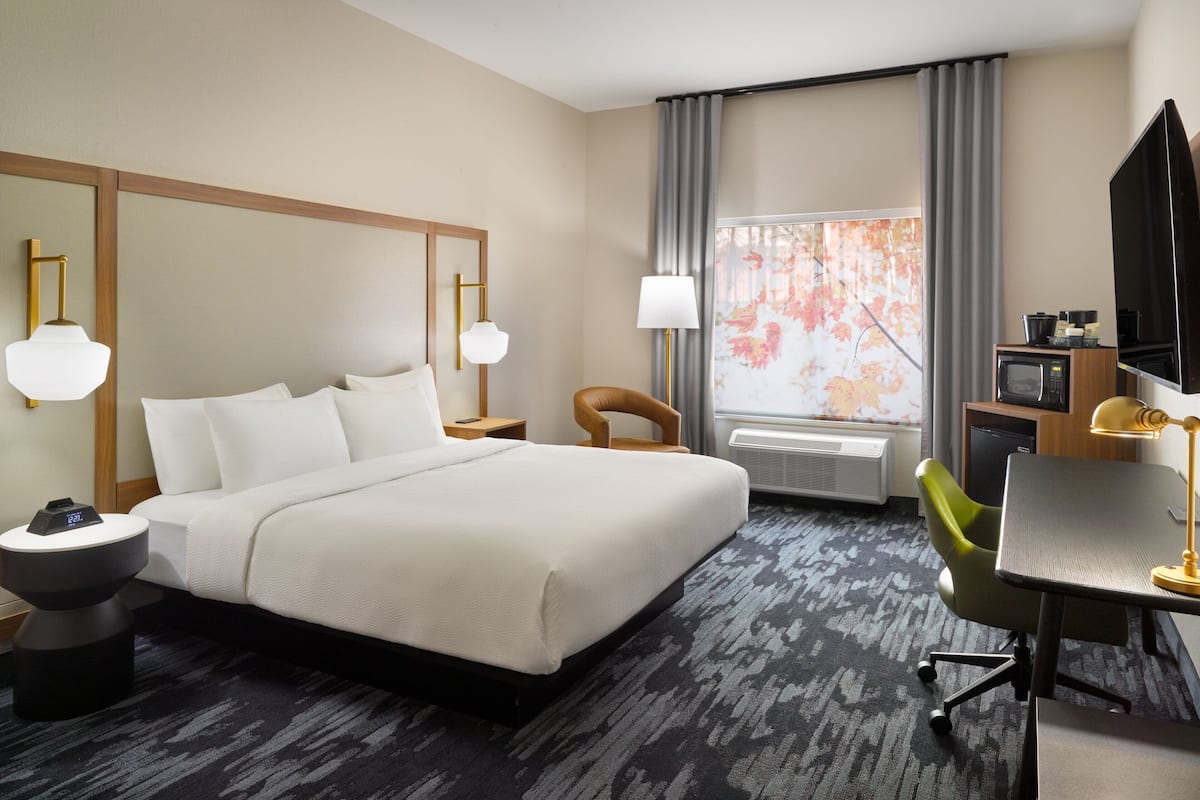 Een hotelkamer met een groot bed, een bureau, een stoel, een televisie en een raam met gordijnen.