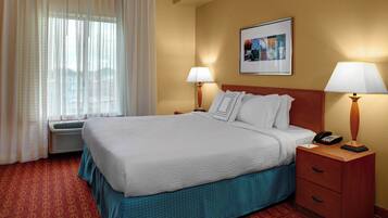 Habitación de hotel con una cama grande, dos mesitas de noche con lámparas, un cuadro en la pared y una ventana con cortinas.