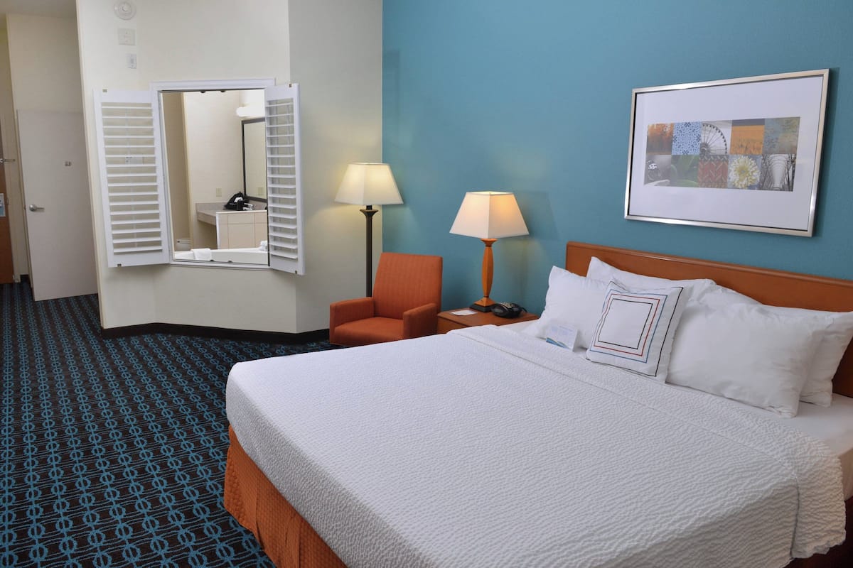 A hotel room with a large bed, two bedside lamps, a chair, a mirror, and a framed picture on the wall.