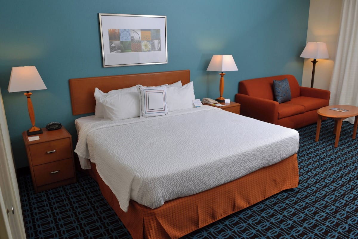 A hotel room with a large bed, two bedside tables, a nightstand, a sofa, and a small round table.